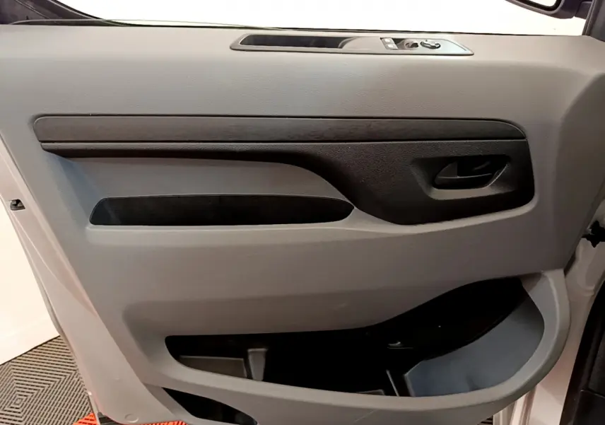 Intérieur côté gauche de la porte avant gris clair du Toyota Proace Verso 2019 avec commandes de vitres et poignée noire.