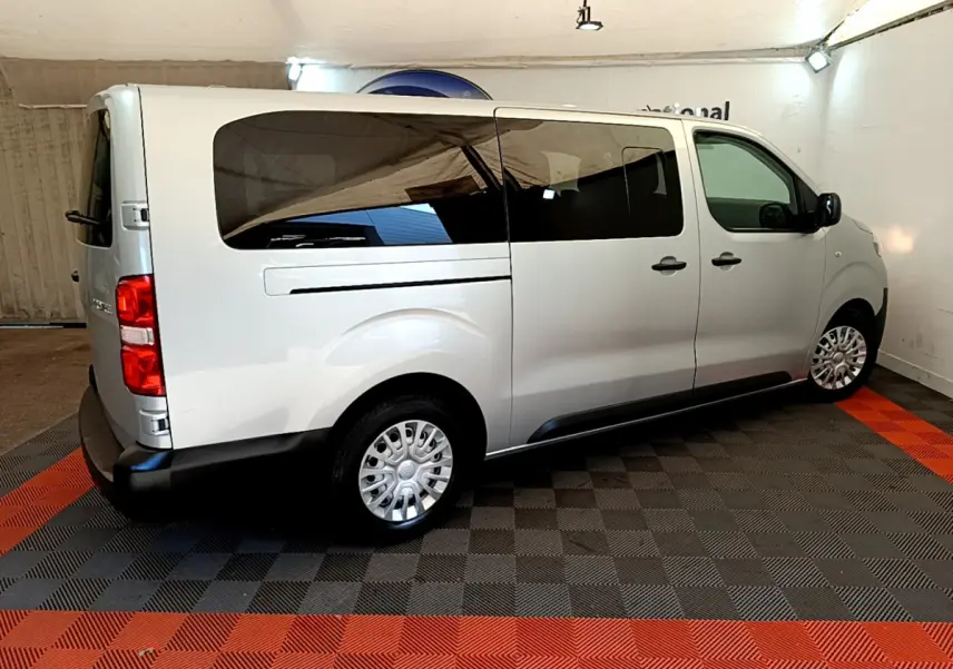 Vue 3/4 arrière droite d'un Toyota Proace Verso gris clair avec vitres teintées et jantes acier en intérieur showroom.