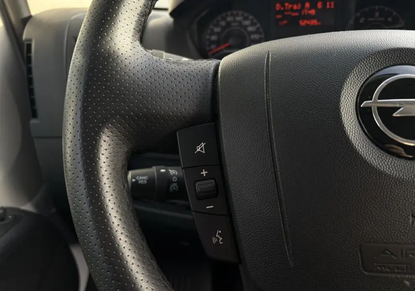 Gros plan sur le volant noir perforé d’un Opel Movano Fourgon 2024 avec commandes intégrées et logo Opel visible.