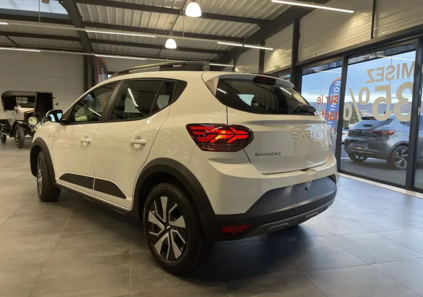 Vue 3/4 arrière droite d'une Dacia Sandero Stepway blanche Glacier avec barres de toit et jantes spécifiques en concession.