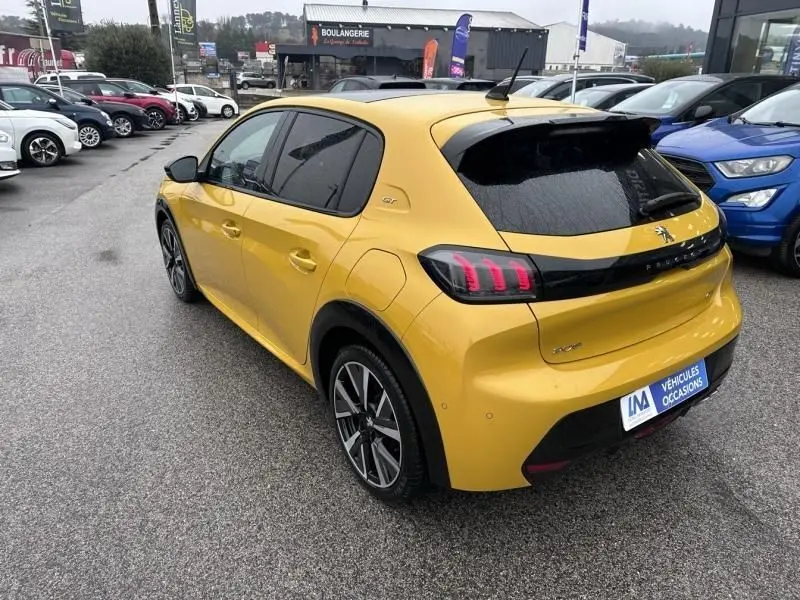 Peugeot 208 jaune vue 3/4 arrière droit, avec feux arrière à griffes et toit noir contrasté, en concession extérieure.