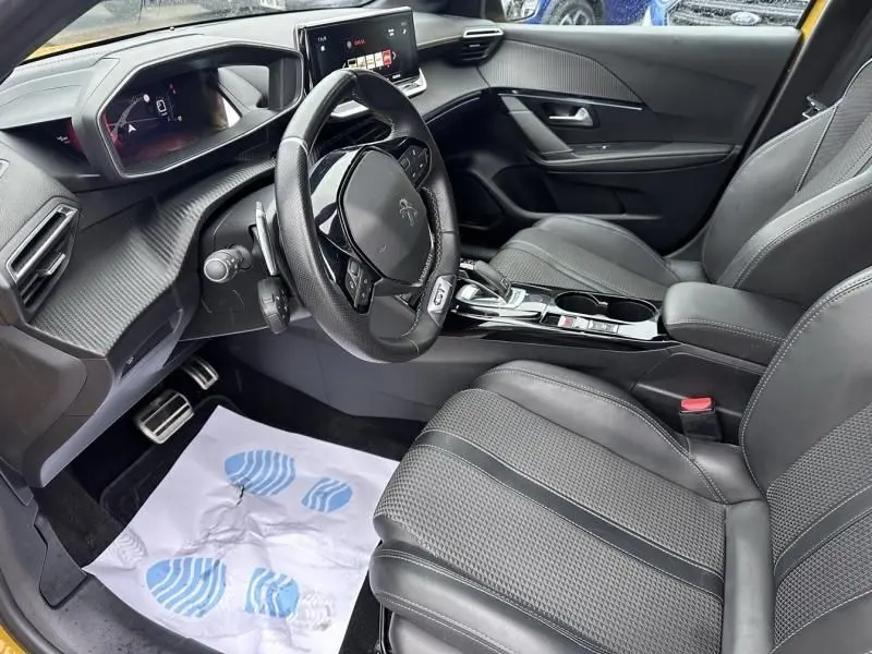 Vue intérieure côté conducteur de la Peugeot 208 GT 1.2 PureTech 130, avec volant compact et sièges en cuir noirs.