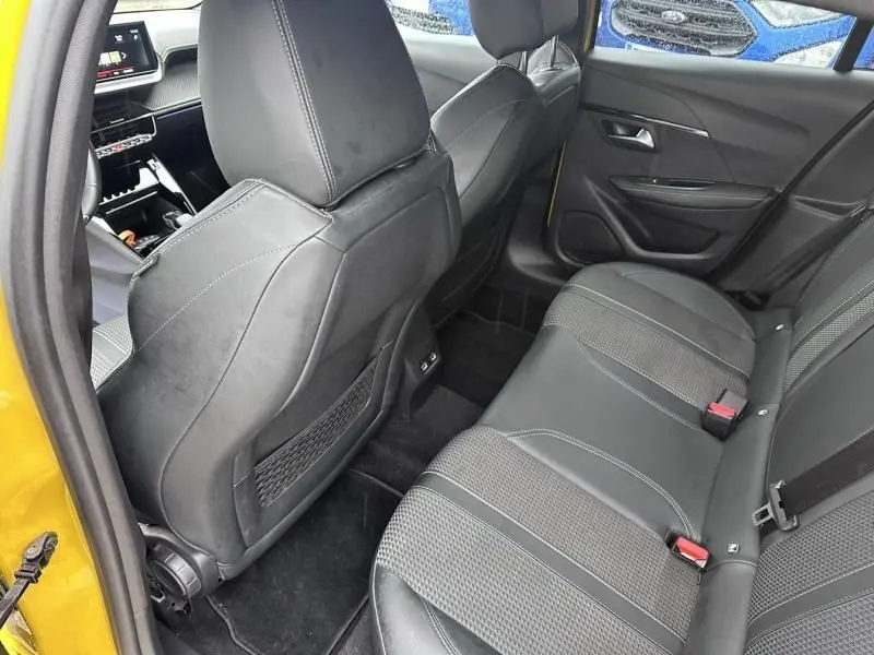 Vue intérieure arrière côté gauche d'une Peugeot 208 jaune 2021, sièges noirs en tissu et cuir avec surpiqûres blanches.