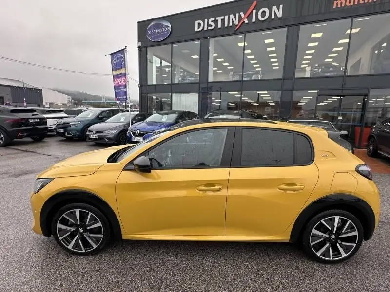Vue de profil côté gauche d’une Peugeot 208 jaune vif 2021, avec jantes alliage et toit noir contrastant.