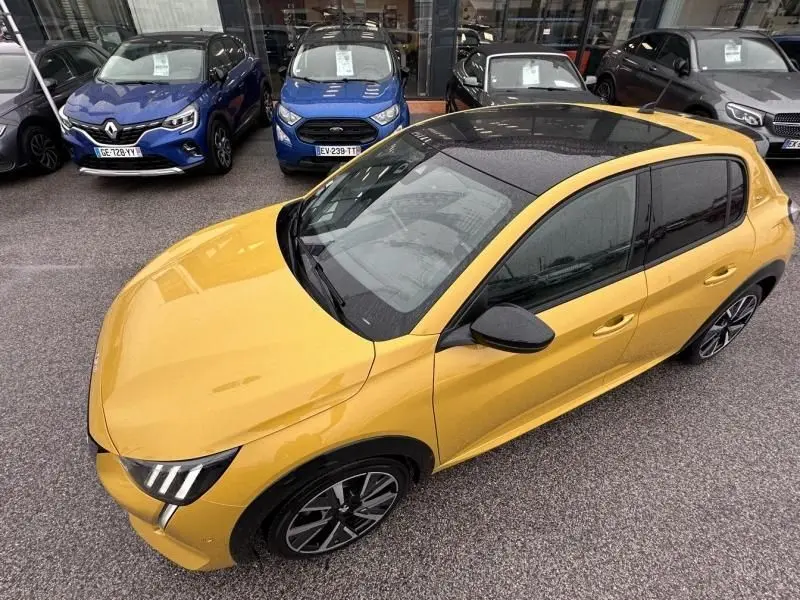 Vue 3/4 avant droit d'une Peugeot 208 jaune avec toit noir et jantes alliage distinctives, stationnée en extérieur.