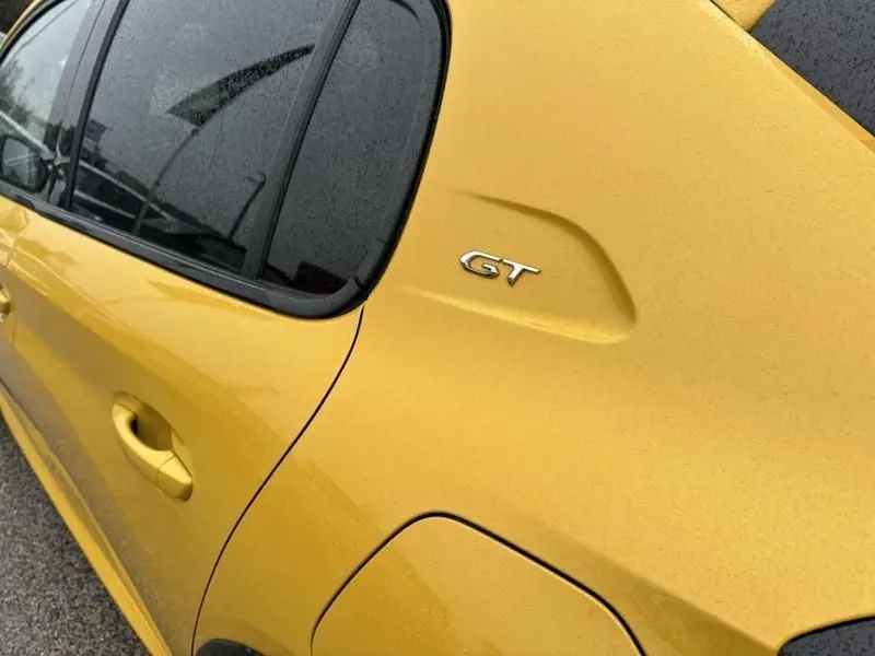 Vue de côté arrière droit d'une Peugeot 208 GT jaune avec logo GT sur l'aile arrière sous la pluie.