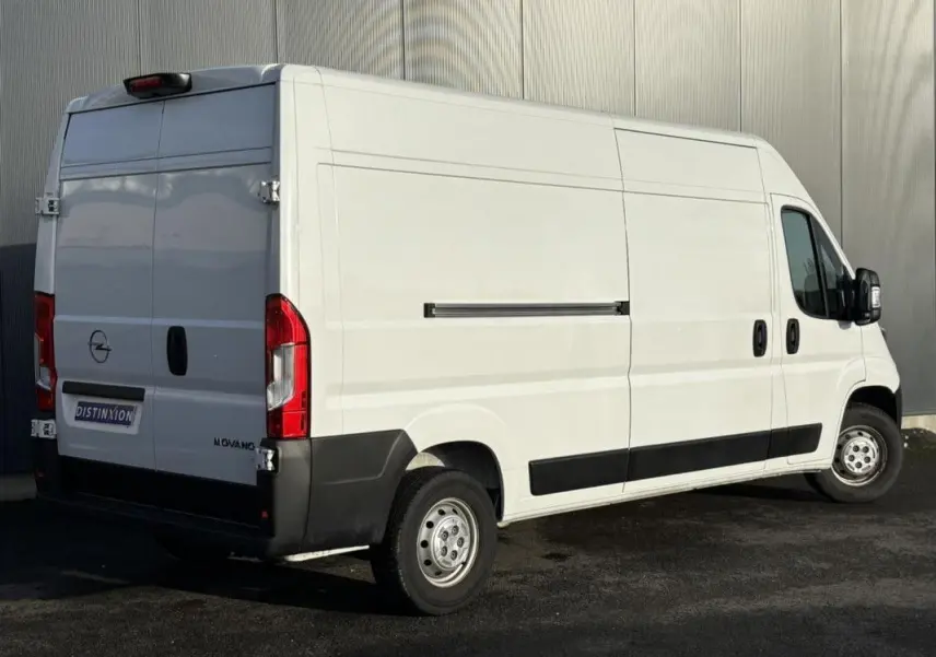 Vue 3/4 arrière droite d’un Opel Movano Fourgon blanc 2023 avec portes arrière battantes et protections noires latérales.