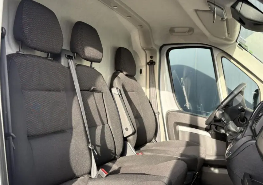 Vue intérieure côté conducteur d’un Opel Movano Fourgon blanc 2023, montrant les sièges avant en tissu gris foncé.