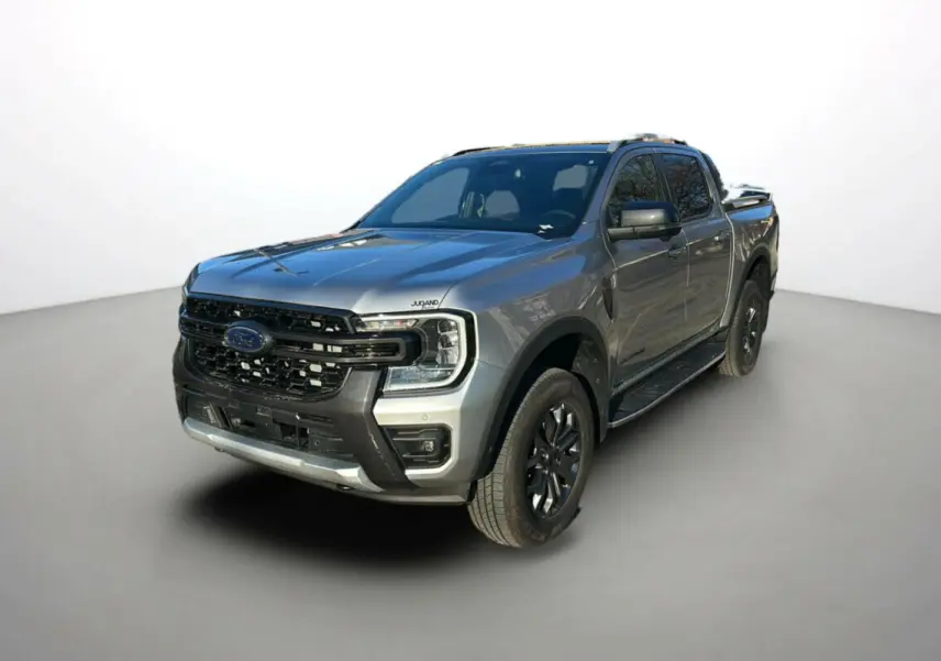 Ford Ranger 2.0 205 Wildtrak Plus gris iconic en 3/4 avant avec jantes alu noires et barres de toit visibles.