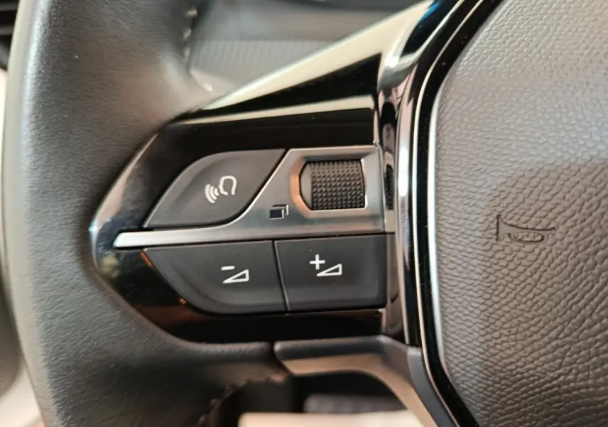 Gros plan sur les commandes gauche du volant cuir multifonctions de la Peugeot 208 électrique blanche, année 2022.