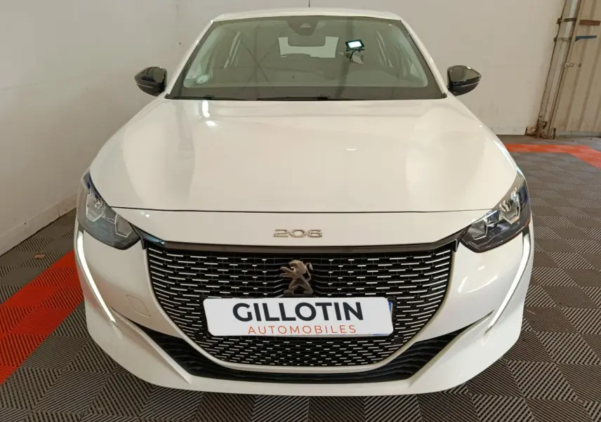 Vue avant d'une Peugeot 208 électrique blanche, avec calandre noire et feux LED distinctifs allumés.