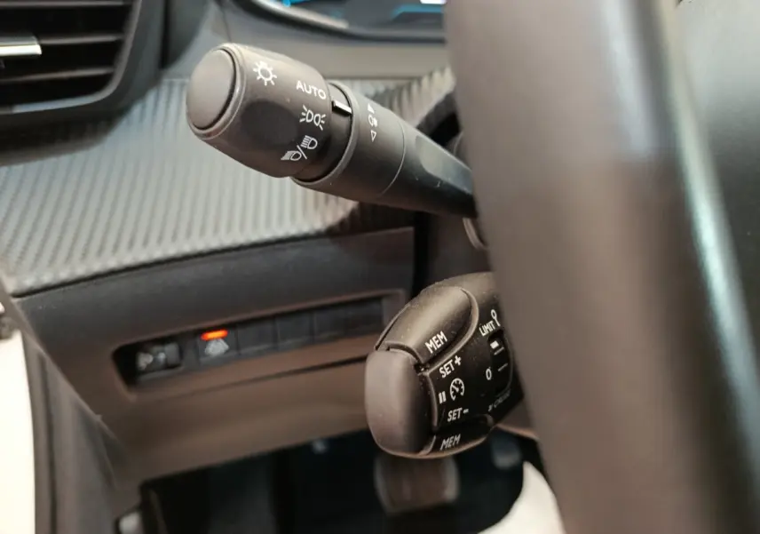 Gros plan sur les commandes au volant noir de la Peugeot 208 électrique Active Business R, tableau de bord en arrière-plan.