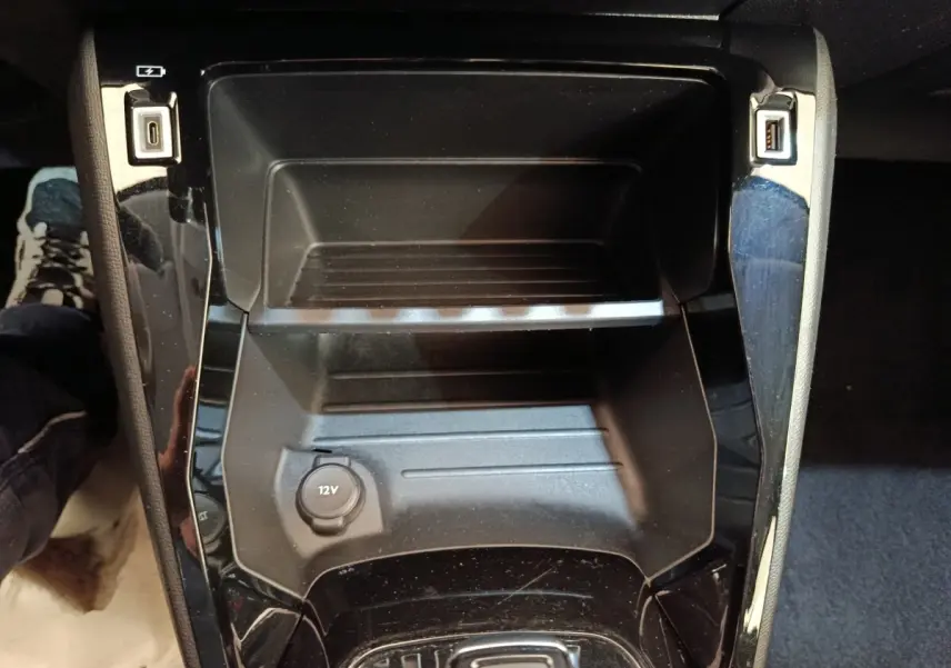 Vue rapprochée de la console centrale noire du Peugeot 208 électrique 2022 avec prise 12V et ports USB visibles.