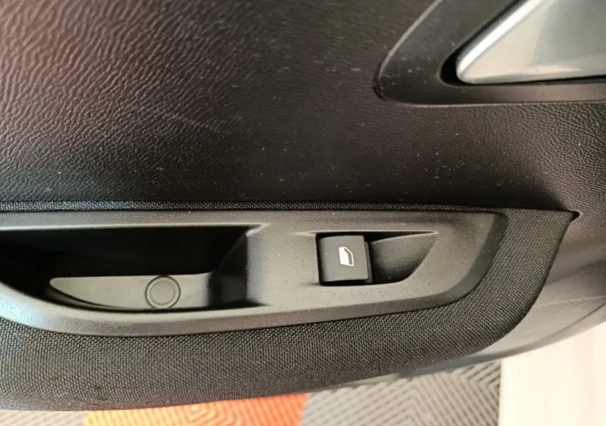 Gros plan sur la commande de lève-vitre électrique côté conducteur de la porte intérieure noire du Peugeot 208 électrique blanc.