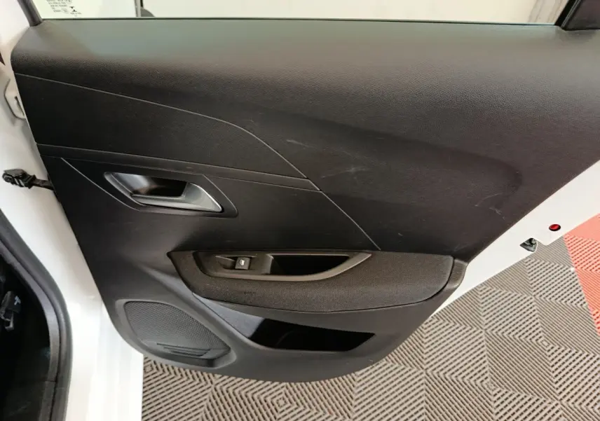 Vue intérieure côté gauche de la porte avant noire d'une Peugeot 208 électrique blanche, avec poignée et commande de vitre.