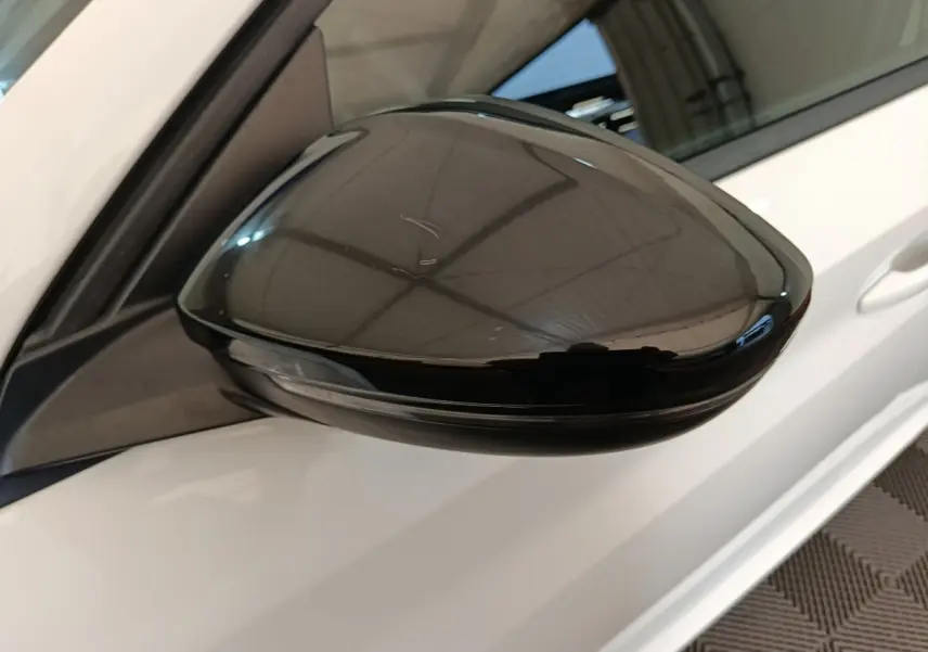 Rétroviseur noir brillant côté conducteur d’une Peugeot 208 électrique blanche vue en gros plan.