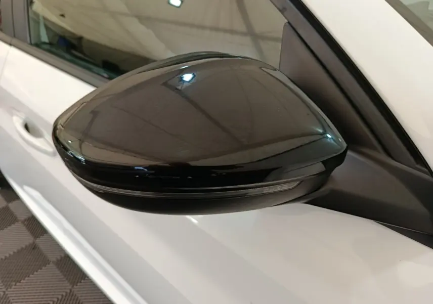 Rétroviseur noir côté gauche sur Peugeot 208 électrique blanche, vue rapprochée en intérieur.
