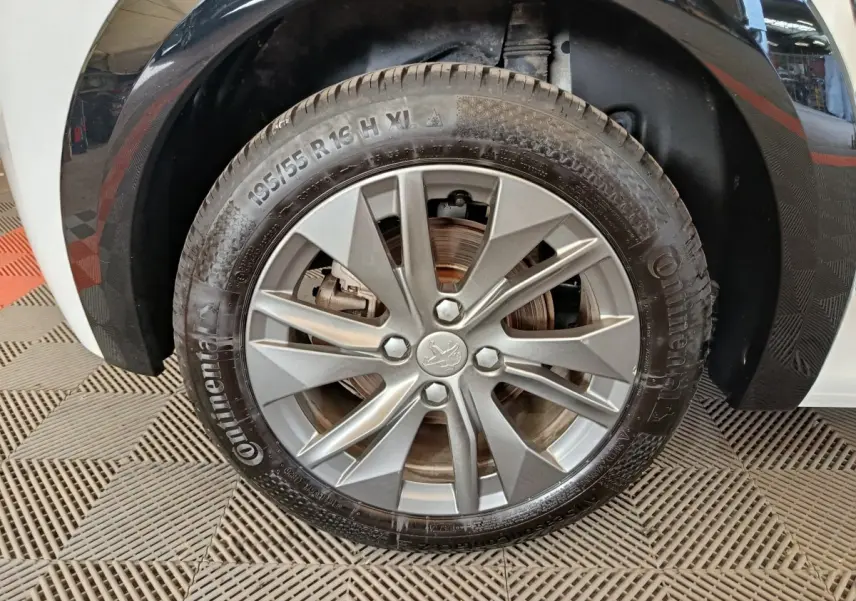 Gros plan sur la roue avant gauche de la Peugeot 208 électrique blanche, avec jante alliage et pneu Continental.