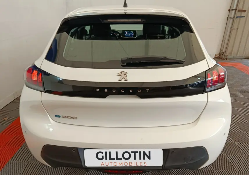 Vue arrière d'une Peugeot 208 électrique blanche avec logo et bande noire distinctive sur le hayon.