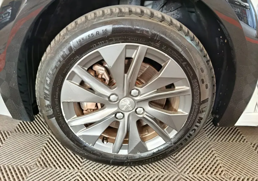 Gros plan sur la roue avant droite d'une Peugeot 208 électrique blanche, jante alliage avec logo Peugeot central.