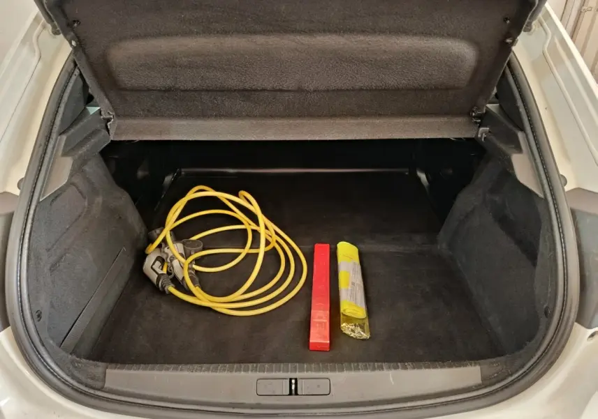 Coffre ouvert d’une Peugeot 208 électrique blanche, montrant un câble de recharge jaune et un triangle de signalisation rouge.