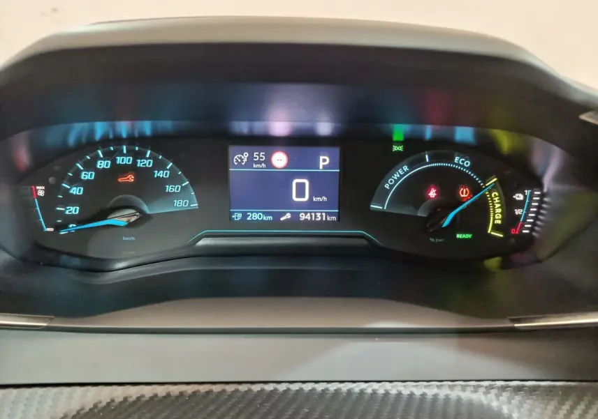 Tableau de bord numérique de Peugeot 208 électrique blanc, affichage vitesse et autonomie, vue frontale rapprochée.