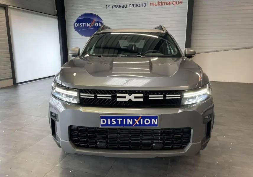 Vue avant du Dacia Bigster gris schiste avec calandre noire et signature lumineuse LED allumée en intérieur showroom.