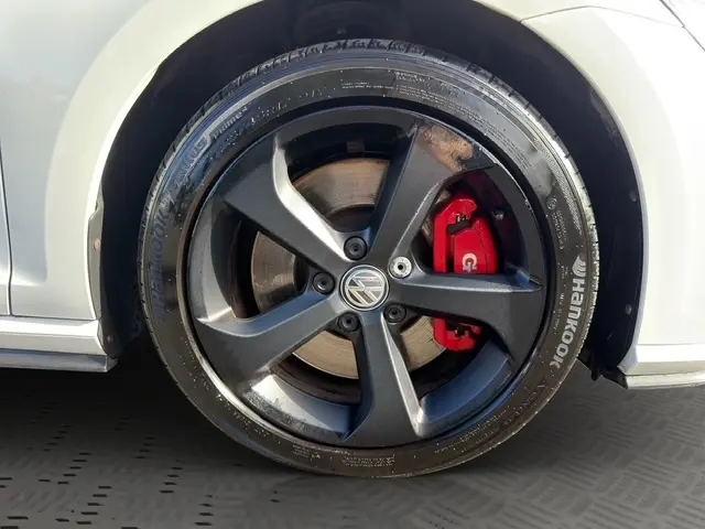 Vue intérieure côté conducteur de la Volkswagen Golf GTI Performance blanche, sièges à motif tartan et volant cuir alu multifonctions.