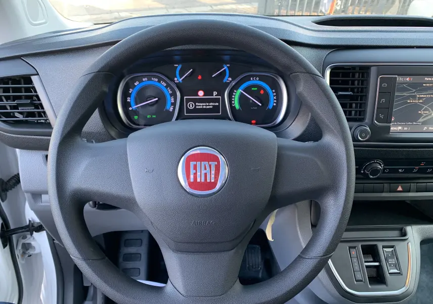 Vue centrée sur le volant noir avec logo FIAT, tableau de bord digital et console centrale d'un FIAT Scudo Combi blanc électrique 2022.