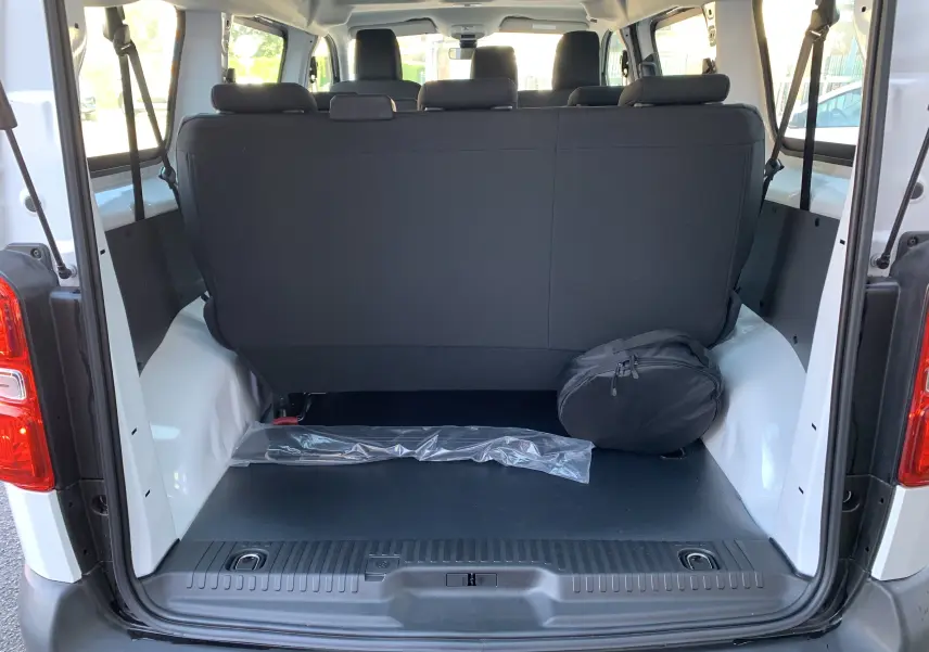 Vue arrière du coffre ouvert d'un FIAT Scudo Combi blanc 2022, montrant les sièges noirs et un sac rond noir posé à droite.