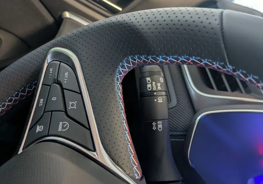 Gros plan sur le volant cuir noir perforé avec surpiqûres tricolores du Renault Symbioz E-Tech 2025, côté gauche.