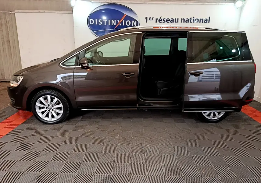 Vue latérale gauche d'un Volkswagen Sharan marron 2017 avec porte coulissante arrière ouverte en intérieur showroom.
