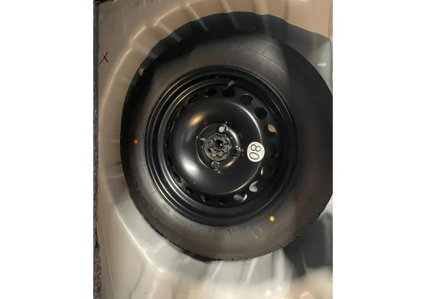 Gros plan sur la roue de secours noire dans le coffre gris clair d'une Dacia Sandero Blanc Glacier 2025.