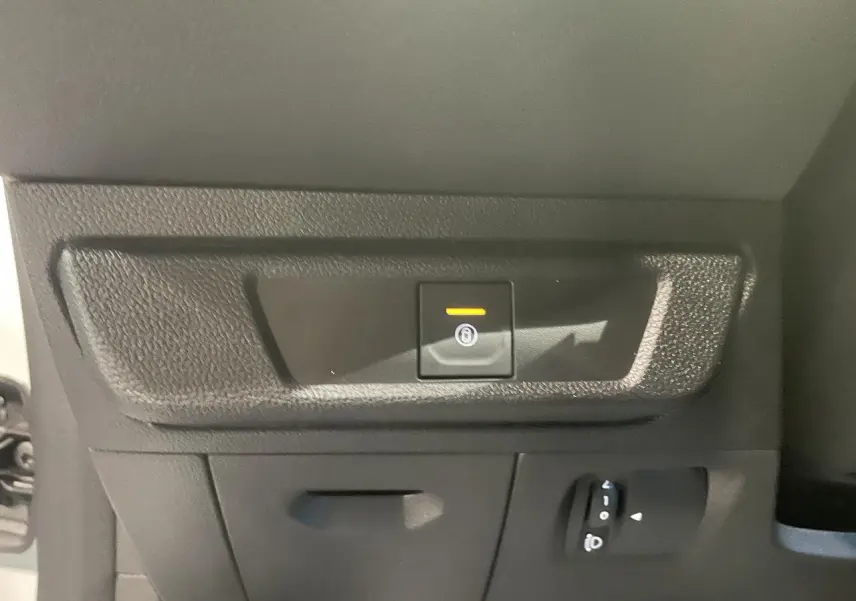 Gros plan sur le bouton de frein de stationnement électrique dans l'habitacle d'une Dacia Sandero blanc glacier 2025.
