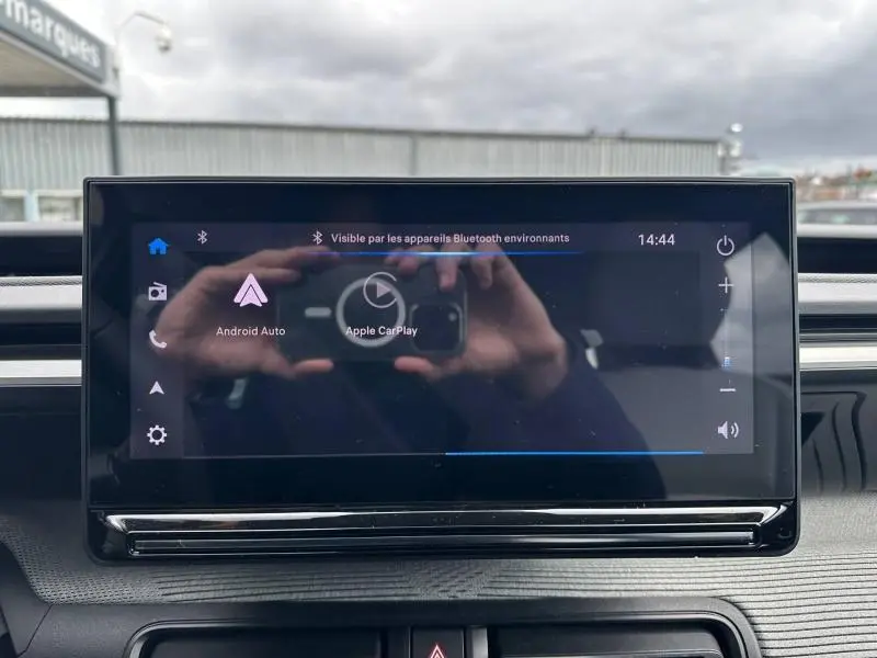 Écran tactile central de la Citroën C3 2025 affichant Android Auto et Apple CarPlay, avec reflet de mains.