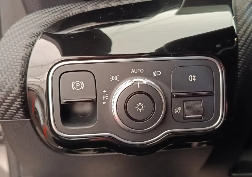 Gros plan sur la commande des phares et frein à main électrique dans l’habitacle noir brillant de la Mercedes Classe A gris clair.