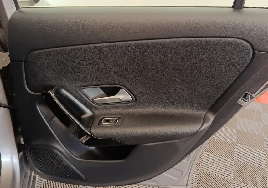 Vue intérieure de la porte avant gauche noire avec poignée argentée et bouton de commande de vitre sur Mercedes Classe A gris clair.