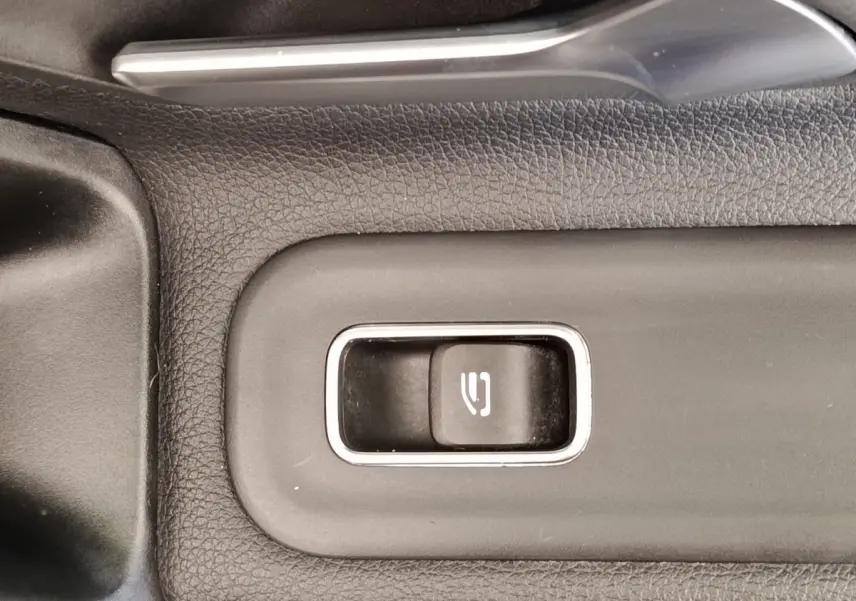 Gros plan sur le bouton de frein à main électrique entouré de plastique noir texturé dans une Mercedes Classe A 180 Business Line.