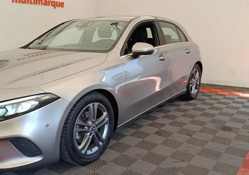 Vue 3/4 avant droit d'une Mercedes Classe A 180 Business Line gris clair, avec jantes alliage et phares LED allumés.