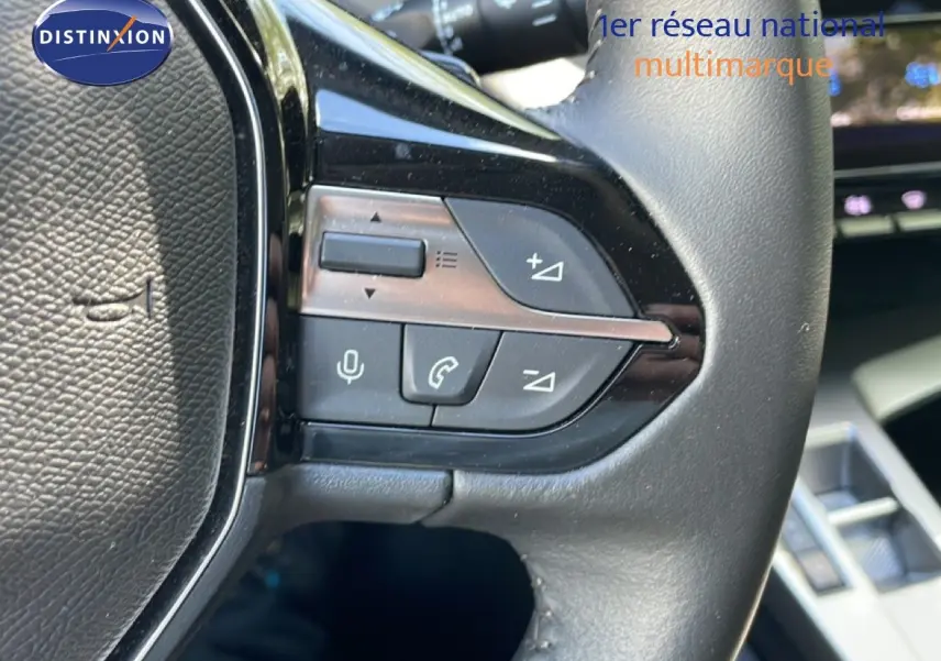 Gros plan sur les commandes au volant en cuir noir de la Peugeot 308 SW Hybrid 145ch, détails des boutons multifonctions.