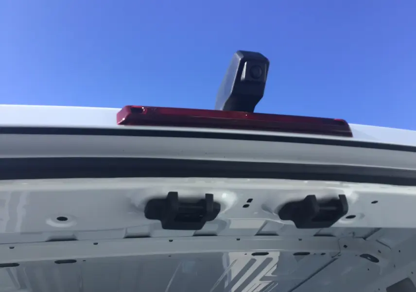 Gros plan sur la caméra de recul et le feu stop rouge au sommet de la porte arrière blanche d'un Renault Master 2025.