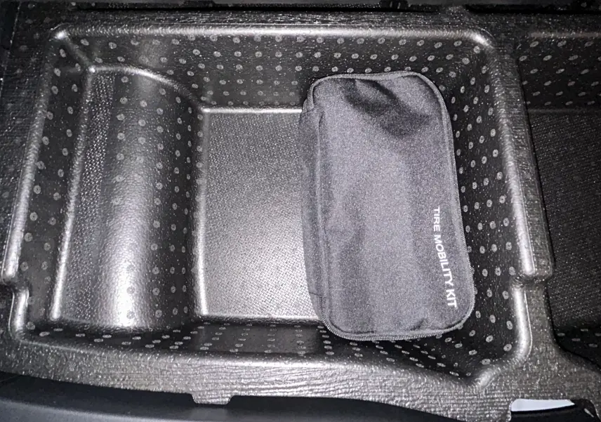 Rangement intérieur du Hyundai Tucson IV Ph.2 STYLE 2025 avec kit de mobilité pneus dans compartiment noir texturé.