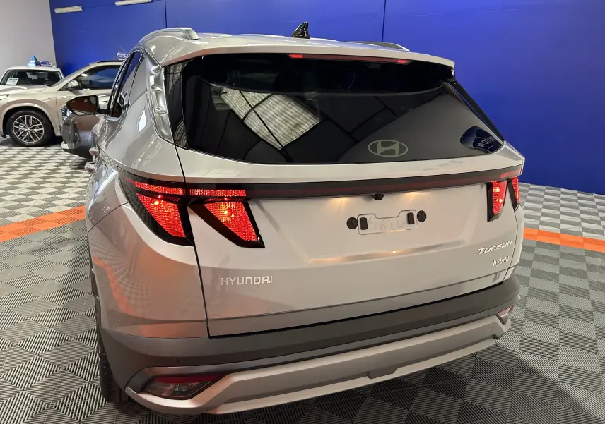 Vue 3/4 arrière d'un Hyundai Tucson 2025 hybride en Shimmering Silver avec vitres arrière surteintées et feux LED allumés.