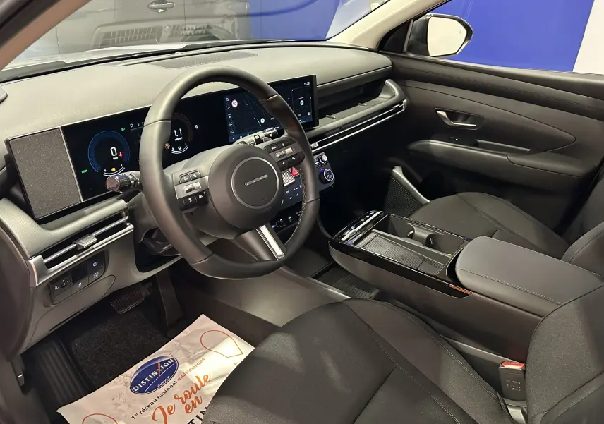 Intérieur du Hyundai Tucson 2025, vue côté conducteur, tableau de bord numérique et sièges tissu noirs visibles.