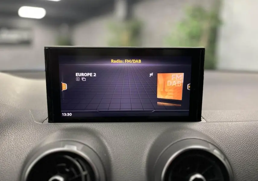 Écran central de l'Audi Q2 2022 affichant la radio FM/DAB, avec tableau de bord noir et aérateurs ronds visibles.
