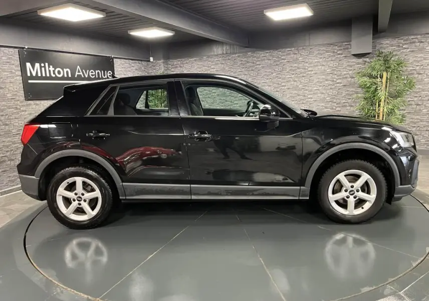 Audi Q2 noir vue de profil côté gauche dans un showroom avec jantes aluminium 16 pouces et peinture vernie brillante.
