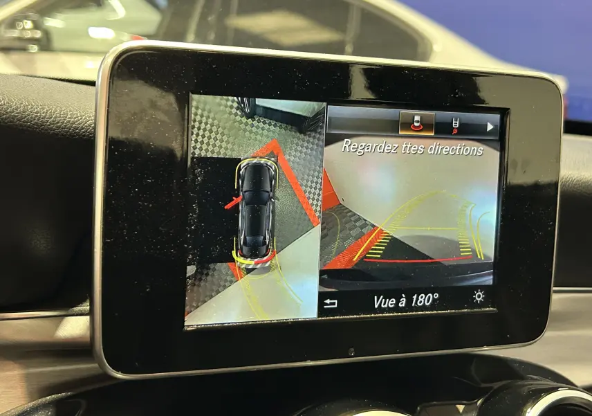 Écran de caméra 360° dans une Mercedes Classe C 200d bleue, affichant vue aérienne et arrière à 180°.
