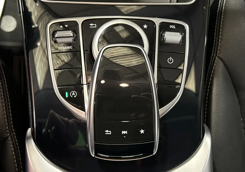 Vue rapprochée de la console centrale noire brillante de la Mercedes Classe C 200d avec commandes tactiles et molette argentée.