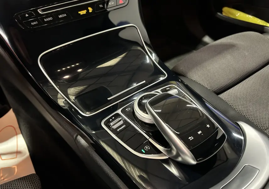Gros plan sur la console centrale noire brillante de la Mercedes Classe C 200d 2018 avec commandes tactiles et molette multimédia.