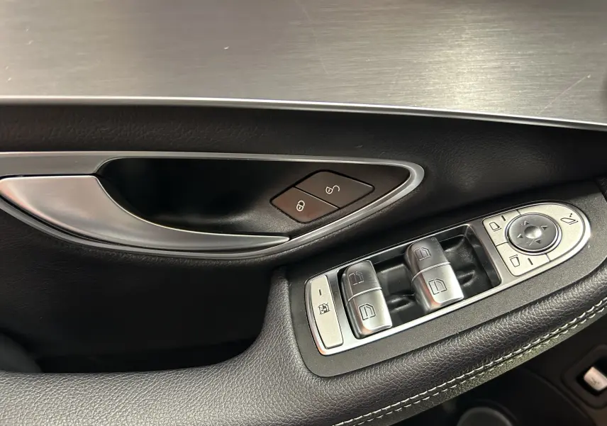 Gros plan sur la commande des vitres et la poignée intérieure côté gauche en cuir noir de la Mercedes Classe C 200d Executive 2018.